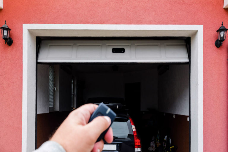A close-up of a hand holding a garage door remote in front of an open garage door.
