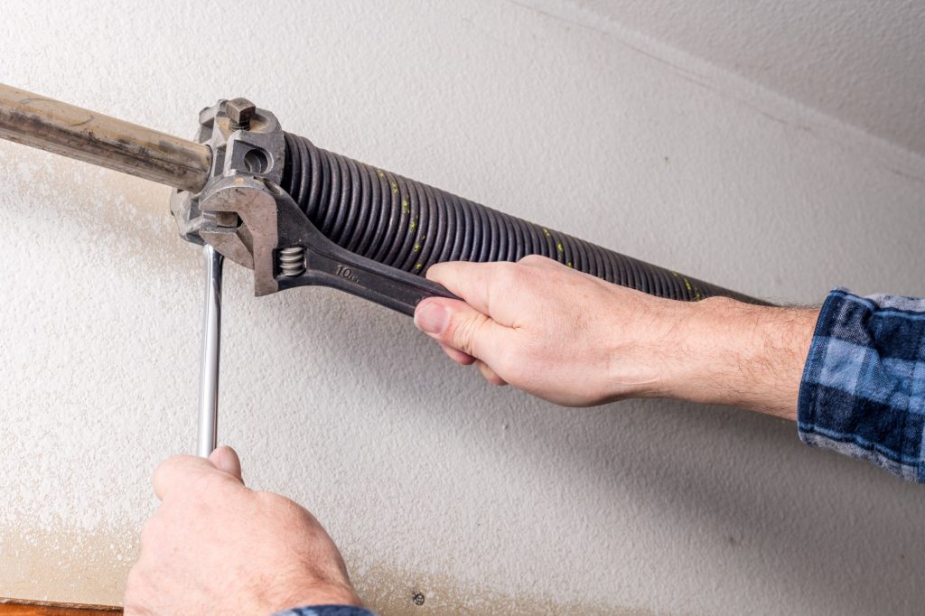 technician using a wrench to tighten a garage door spring