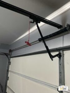 Close-up of a red emergency release cord attached to a garage door opener rail for manual operation.