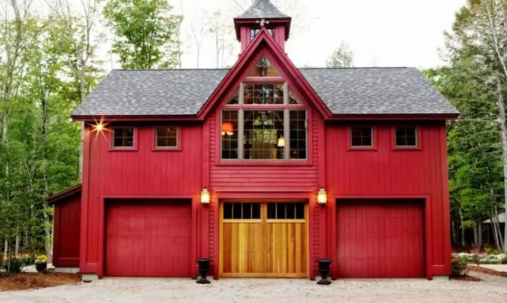 Red carriage house style garage doors on a rustic home surrounded by trees